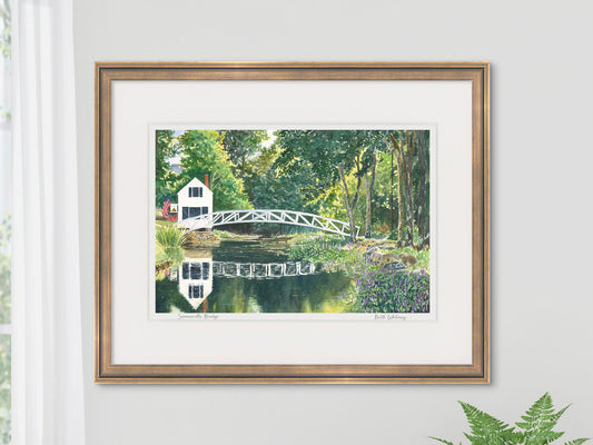 Framed watercolor print of Somesville Bridge, Somesville, Maine, in a gold frame on a cozy wall with a window and fern.