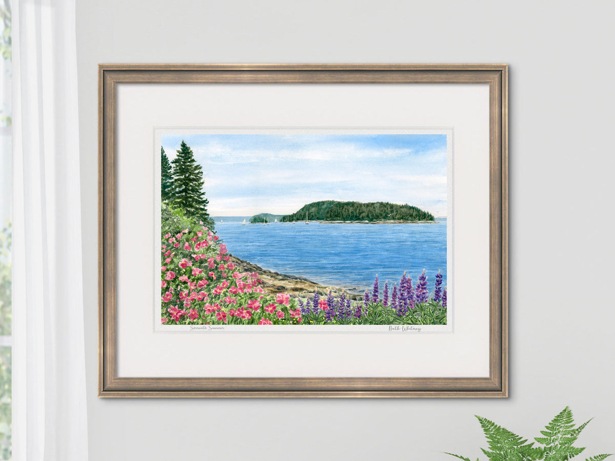 Framed watercolor print of Sorrento Summer, Sorrento, Maine, in a warm gold frame on a neutral wall with a fern.