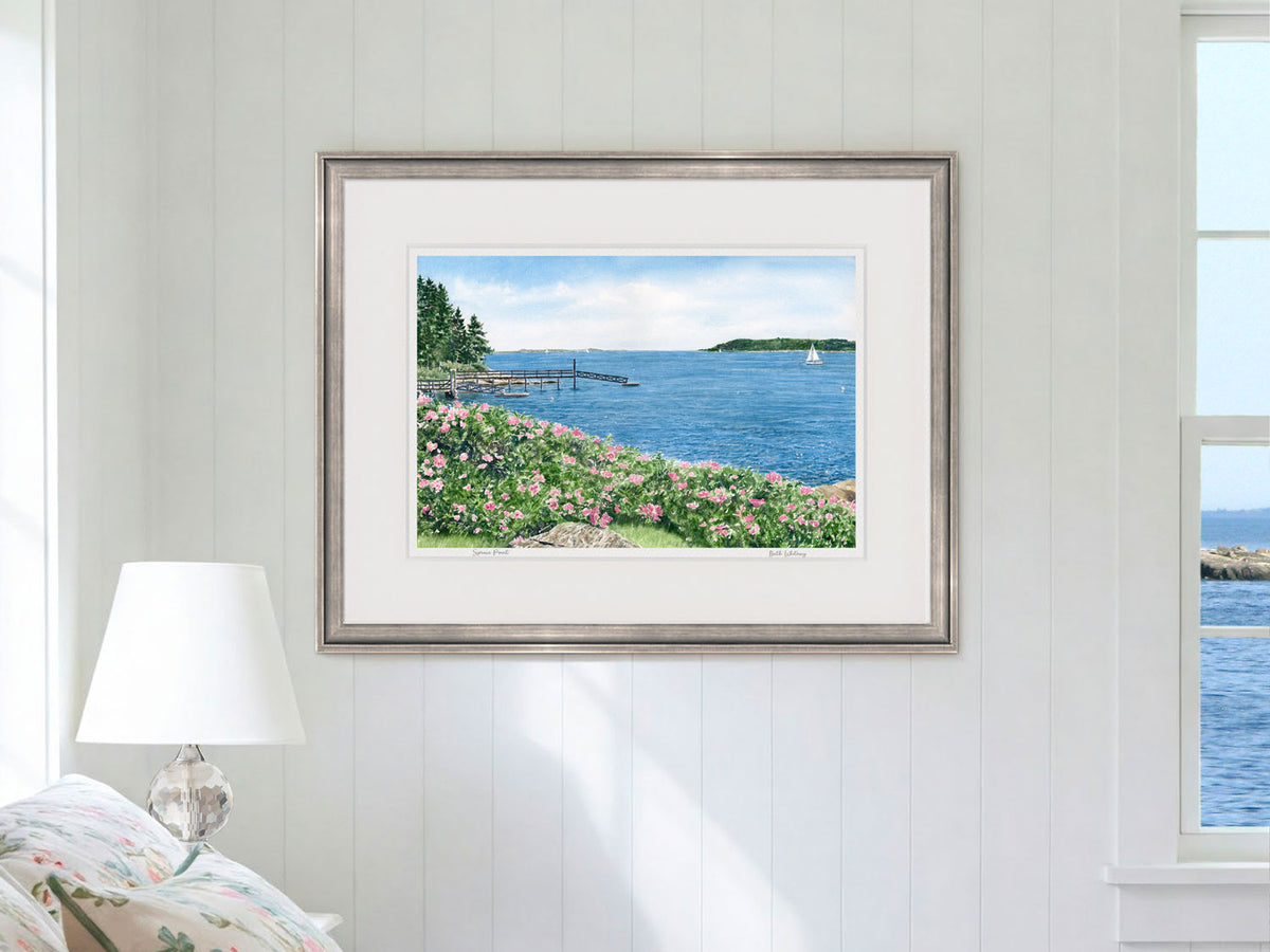 Framed watercolor print of Spruce Point, Boothbay Harbor, Maine, in a silver frame in a bedroom lifestyle setting.