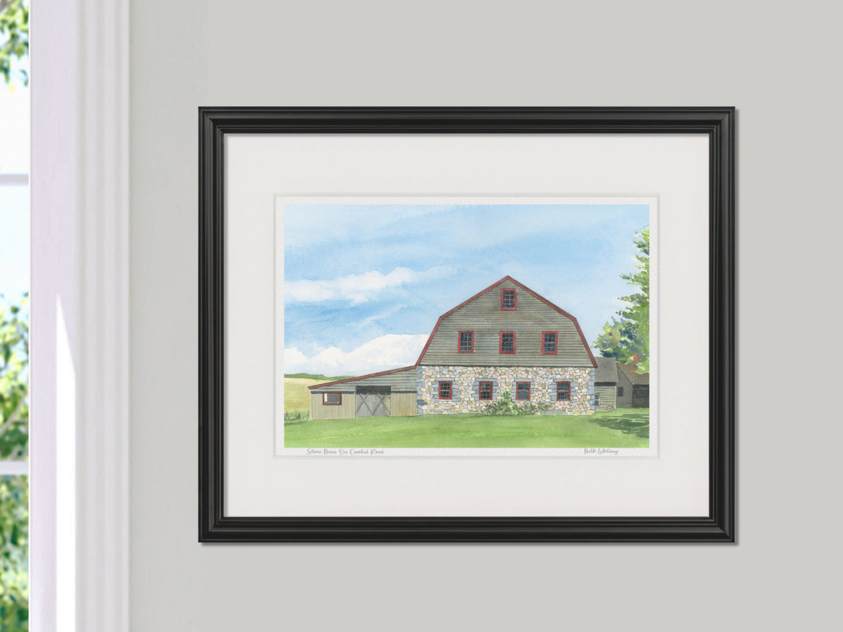 Framed watercolor print of Stone Barn on Crooked Road, Bar Harbor, Maine, in a black frame beside a sunny window.