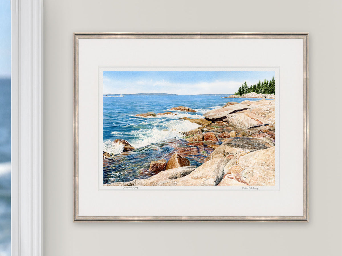 Framed watercolor print of Sunset Surf, East Penobscot Bay, Maine, in a rose gold frame beside a window with an ocean view.