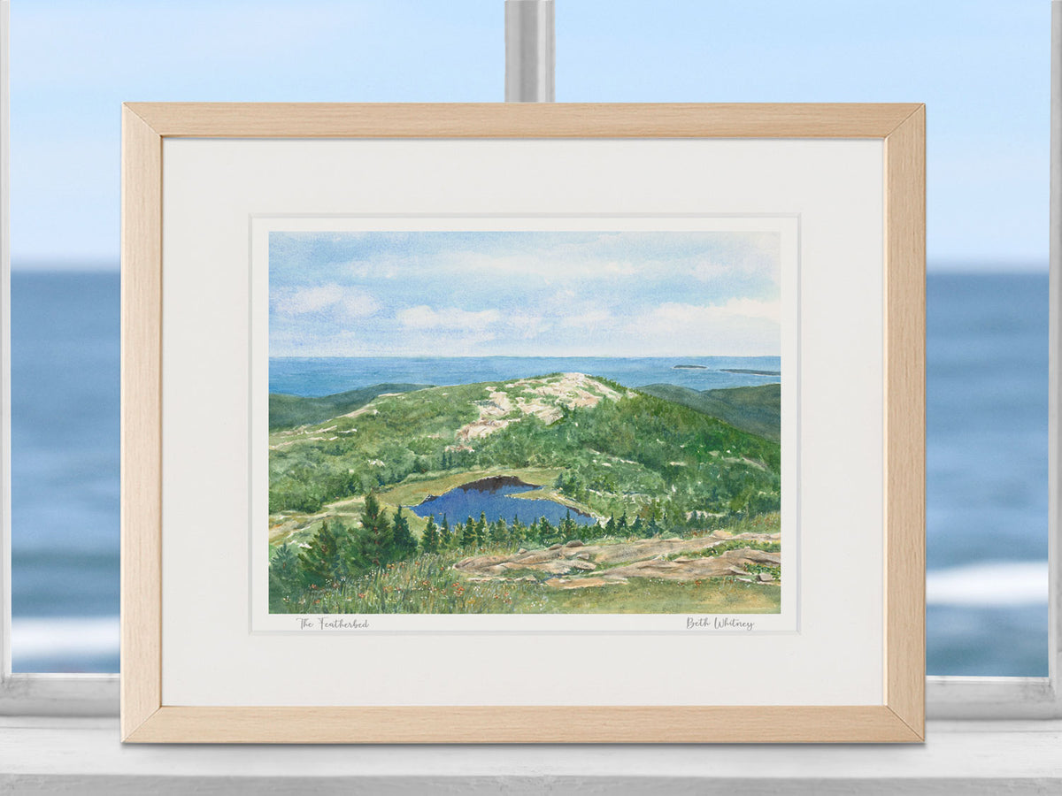Framed watercolor print of The Featherbed, Acadia National Park, in a warm wood frame in a coastal window setting.