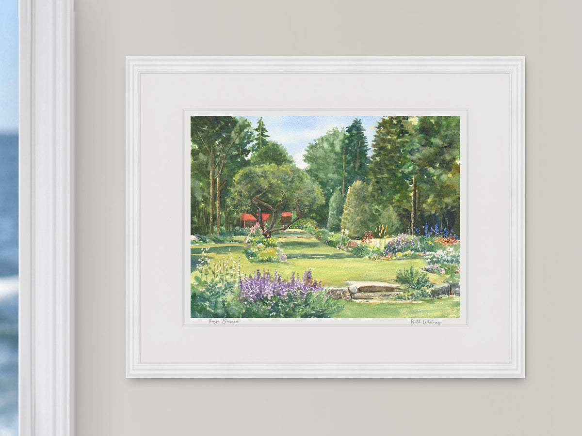 Framed watercolor print of Thuya Garden, Northeast Harbor, Maine, in a white frame beside a window with an ocean view.