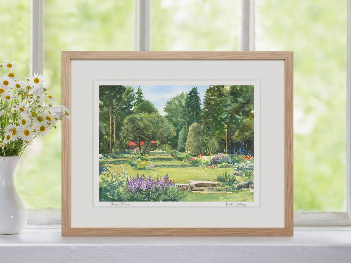 Framed watercolor print of Thuya Garden, Mount Desert Island, Maine, in a warm wood frame in a window setting with flowers.