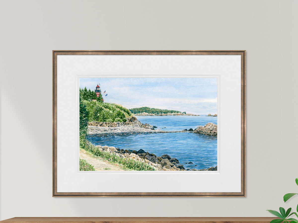 Framed original watercolor painting of West Quoddy Head Light, Lubec, Maine, in a gold frame in a sunny lifestyle setting.