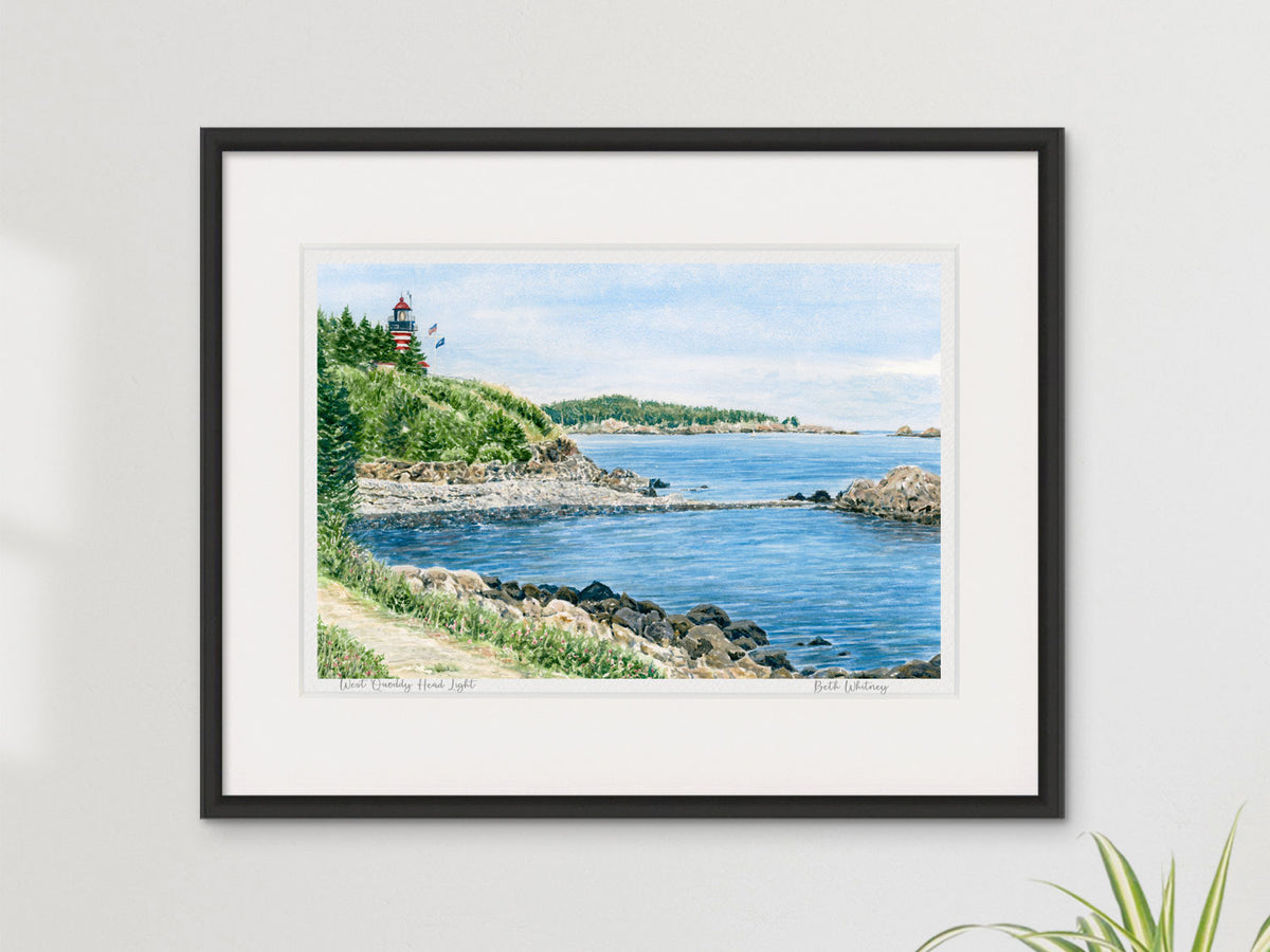 Framed watercolor print of West Quoddy Head Light, Lubec, Maine, in a black frame on a sunny neutral wall.