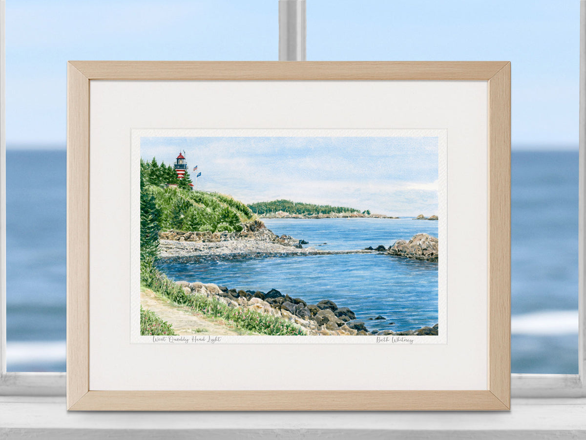 Framed watercolor print of West Quoddy Head Light, Lubec, Maine, in a wood frame in a coastal window decor.