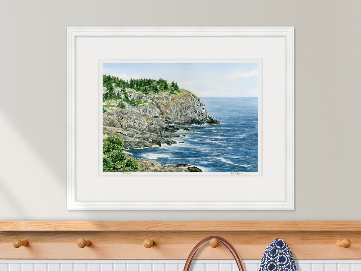 Framed watercolor print of Whitehead, Monhegan Island, in a white frame over a nautical styled entryway coat rack decor.