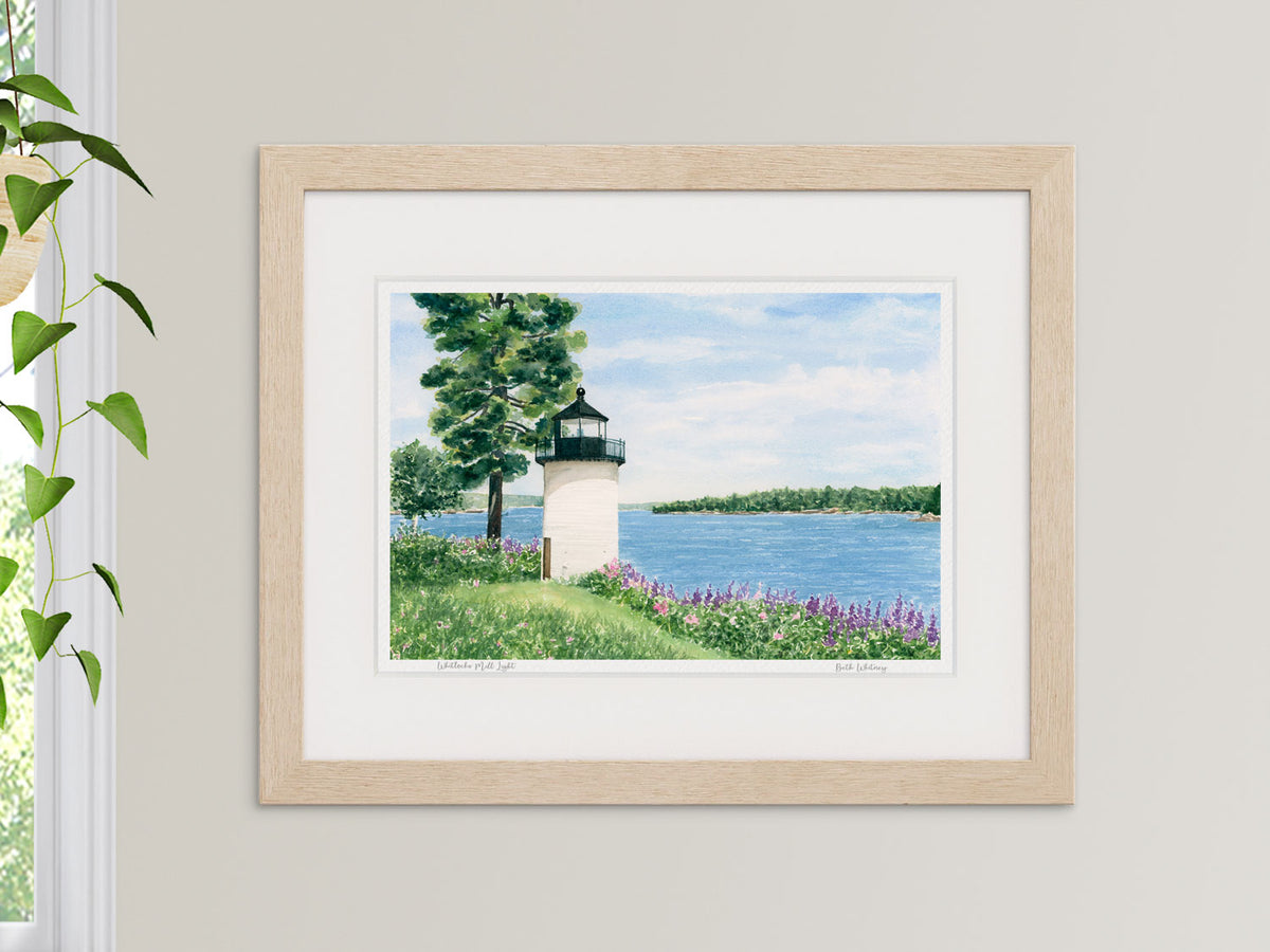 Framed watercolor print of Whitlocks Mill Light, St. Croix River, Maine, in a wood frame beside a window with a hanging plant.