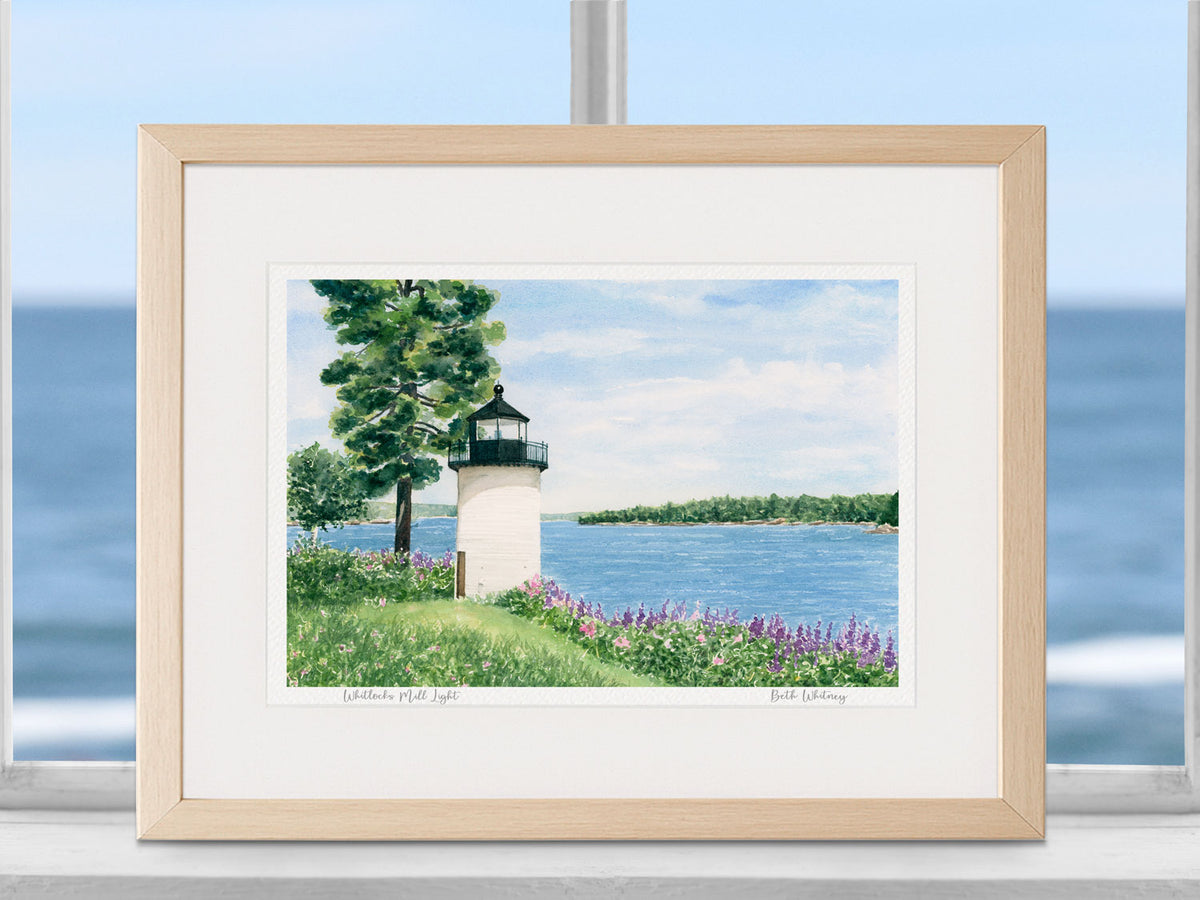 Framed watercolor print of Whitlocks Mill Light, Downeast Maine, in a natural wood frame in a coastal window setting.