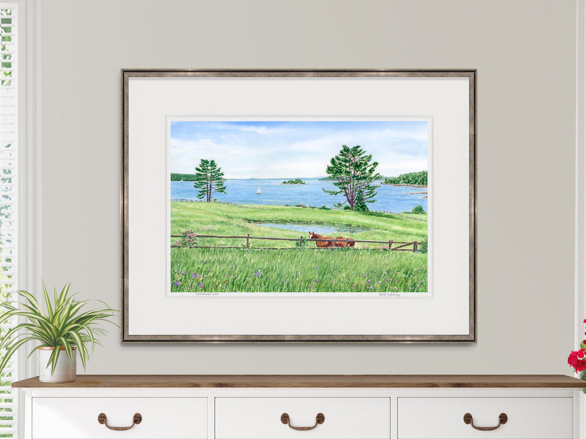 Framed watercolor print of Windswept View, East Blue Hill, Maine, in a black frame on a dresser in a lifestyle setting.