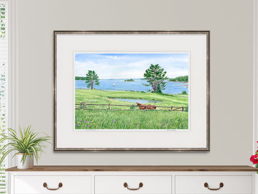 Framed watercolor print of Windswept View, East Blue Hill, Maine, in a black frame on a dresser in a lifestyle setting.