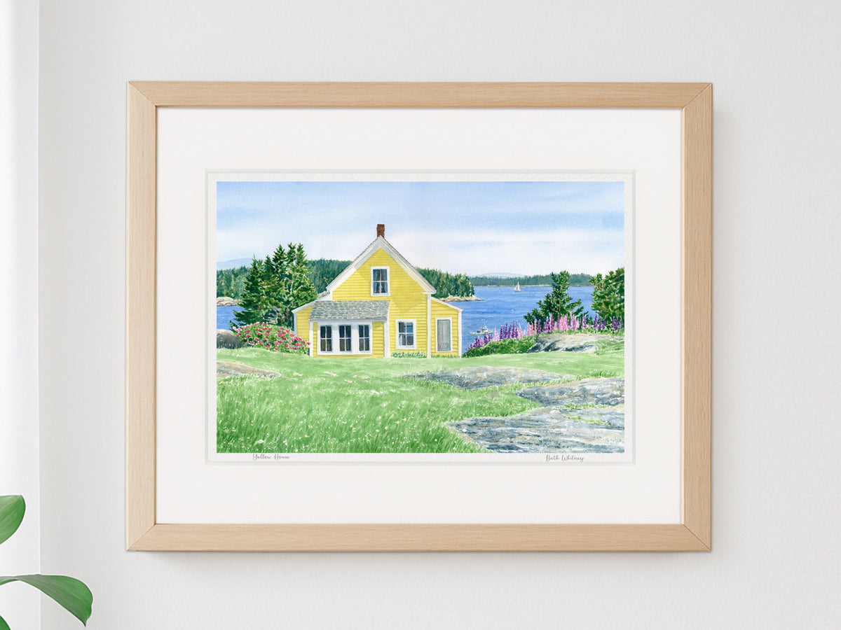 Framed watercolor print of Yellow House, Stonington, Maine, in a warm wood frame on a neutral wall.