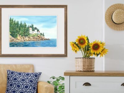 Watercolor painting print of Bass Harbor lighthouse in Maine in a living room with sunflowers and a sofa.