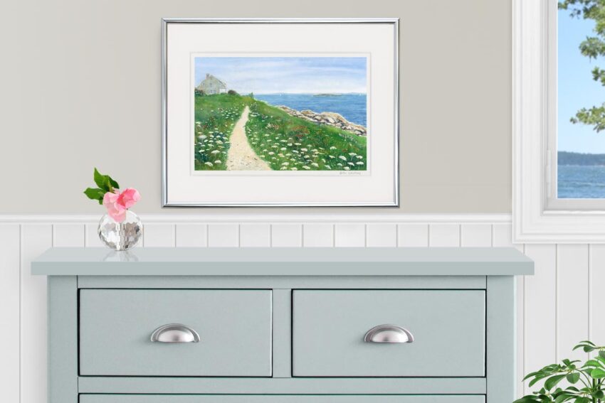 Watercolor of seaside cottage with path along the ocean, winding through grass and wildflowers, shown over a gray dresser.