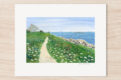 Watercolor of seaside cottage with path along the ocean, winding through grass and wildflowers
