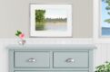 Watercolor painting of a moose at the edge of a pond with trees. Shown over a gray dresser.