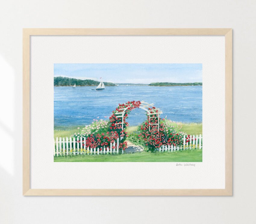 White arbor with picket fence covered in red roses beside the ocean.
