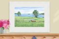 Watercolor of horses in a green pasture with pond, wildflowers, and ocean view.